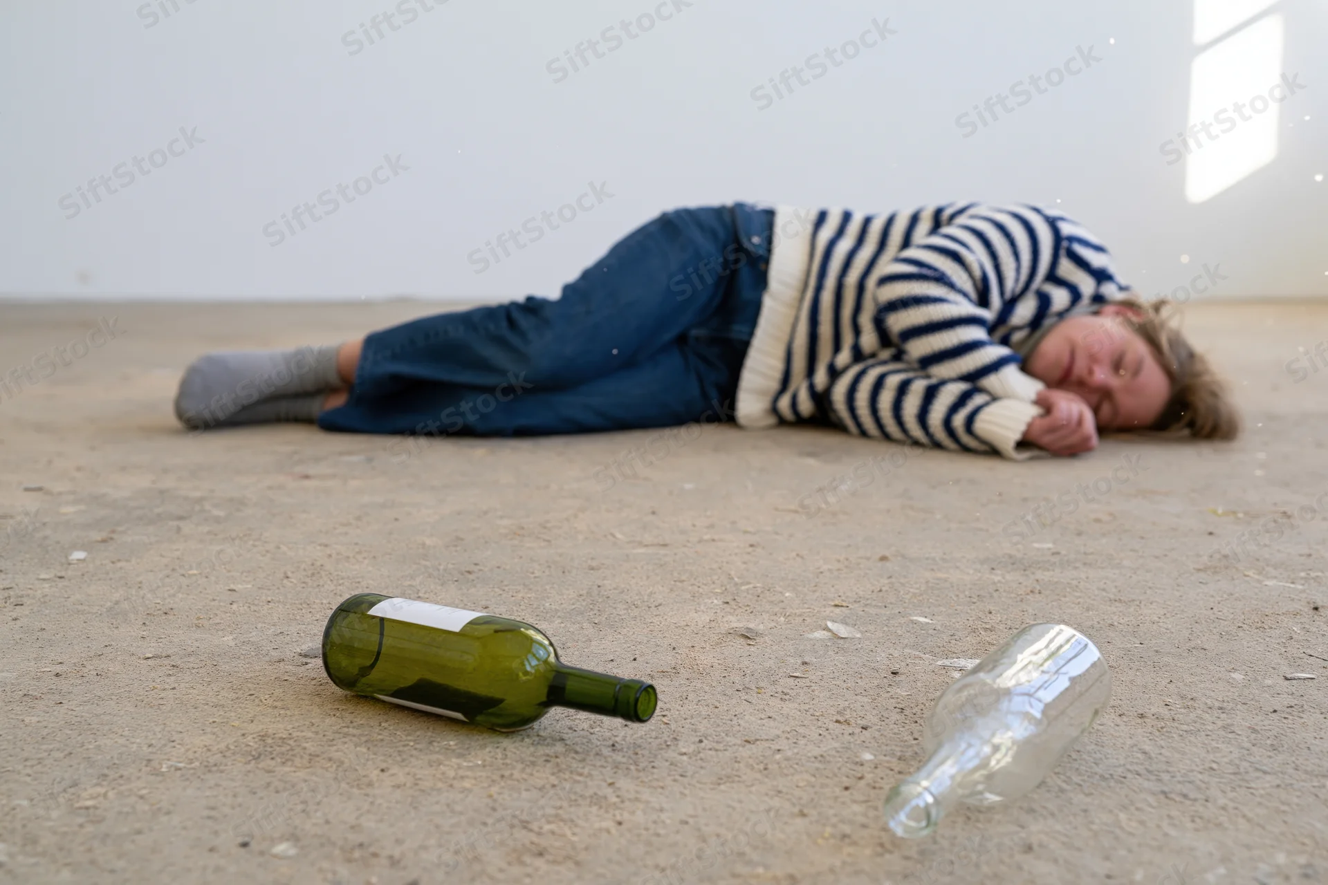 Woman lying unconscious on concrete floor beside empty and broken wine bottles