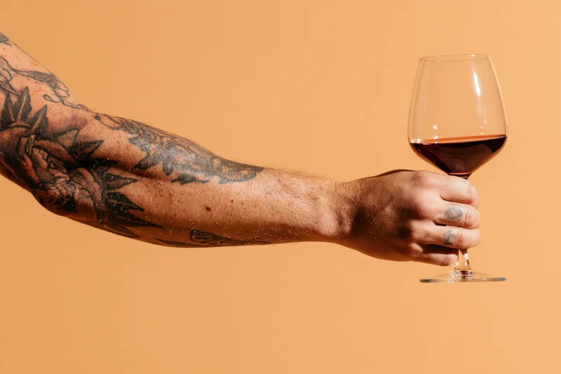 Tattooed arm holding a glass of red wine against orange background