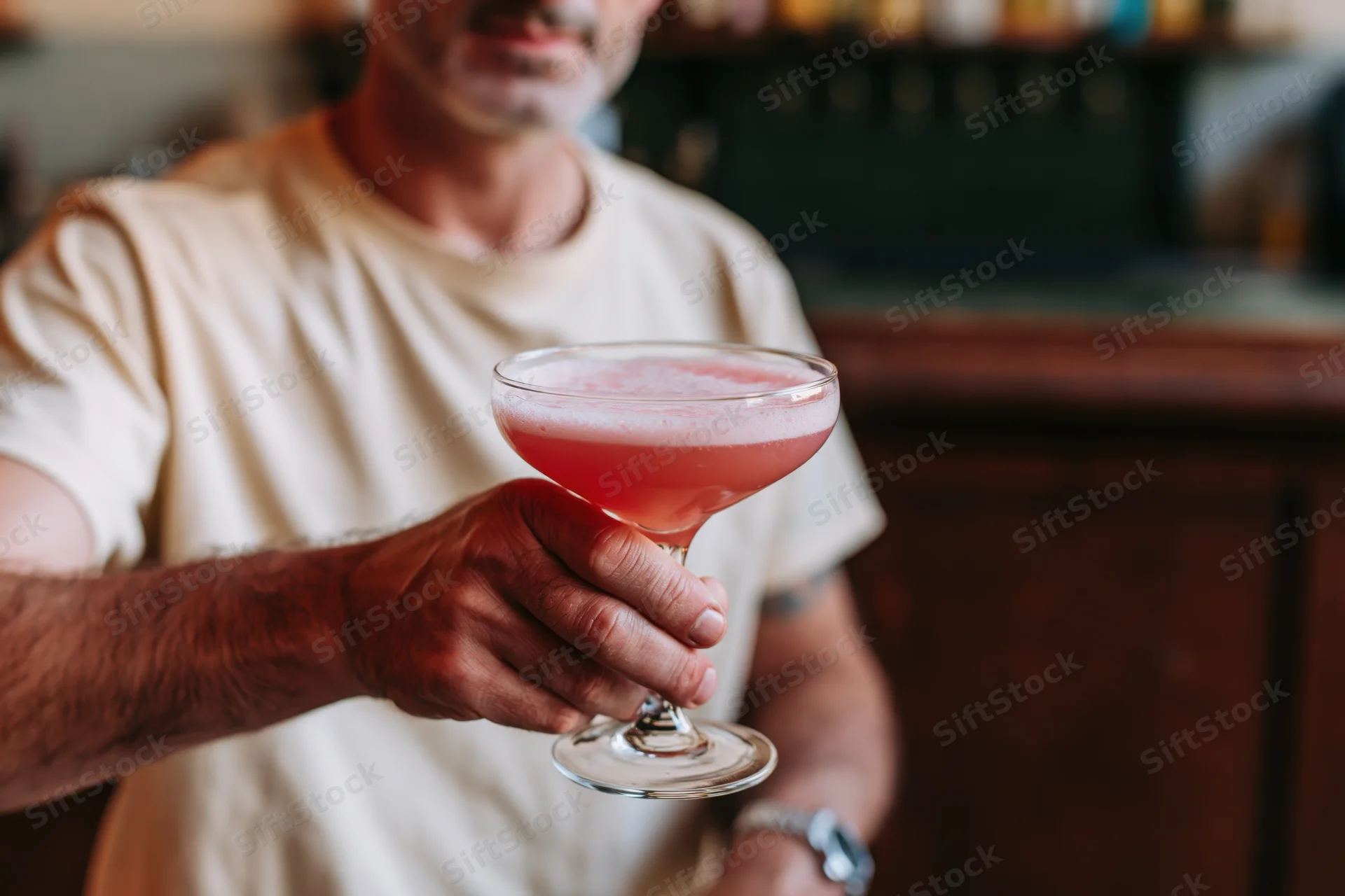 Bartender holding a pink frothy cocktail in a stemmed glass at a bar