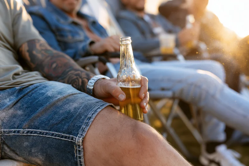 Man holding a beer bottle while relaxing outdoors with friends at sunset