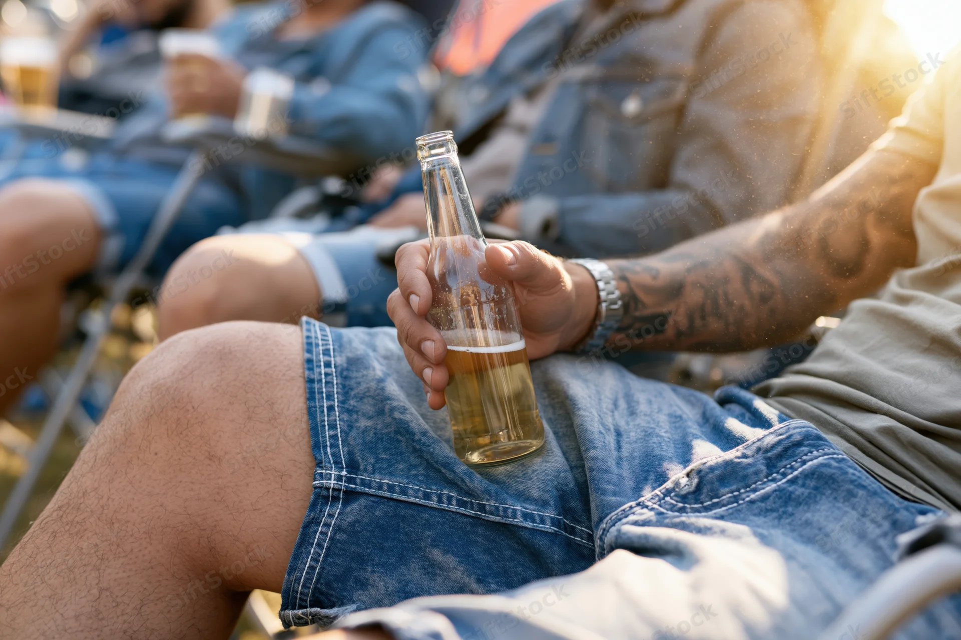 Man holding a beer bottle while relaxing outdoors with friends on folding chairs