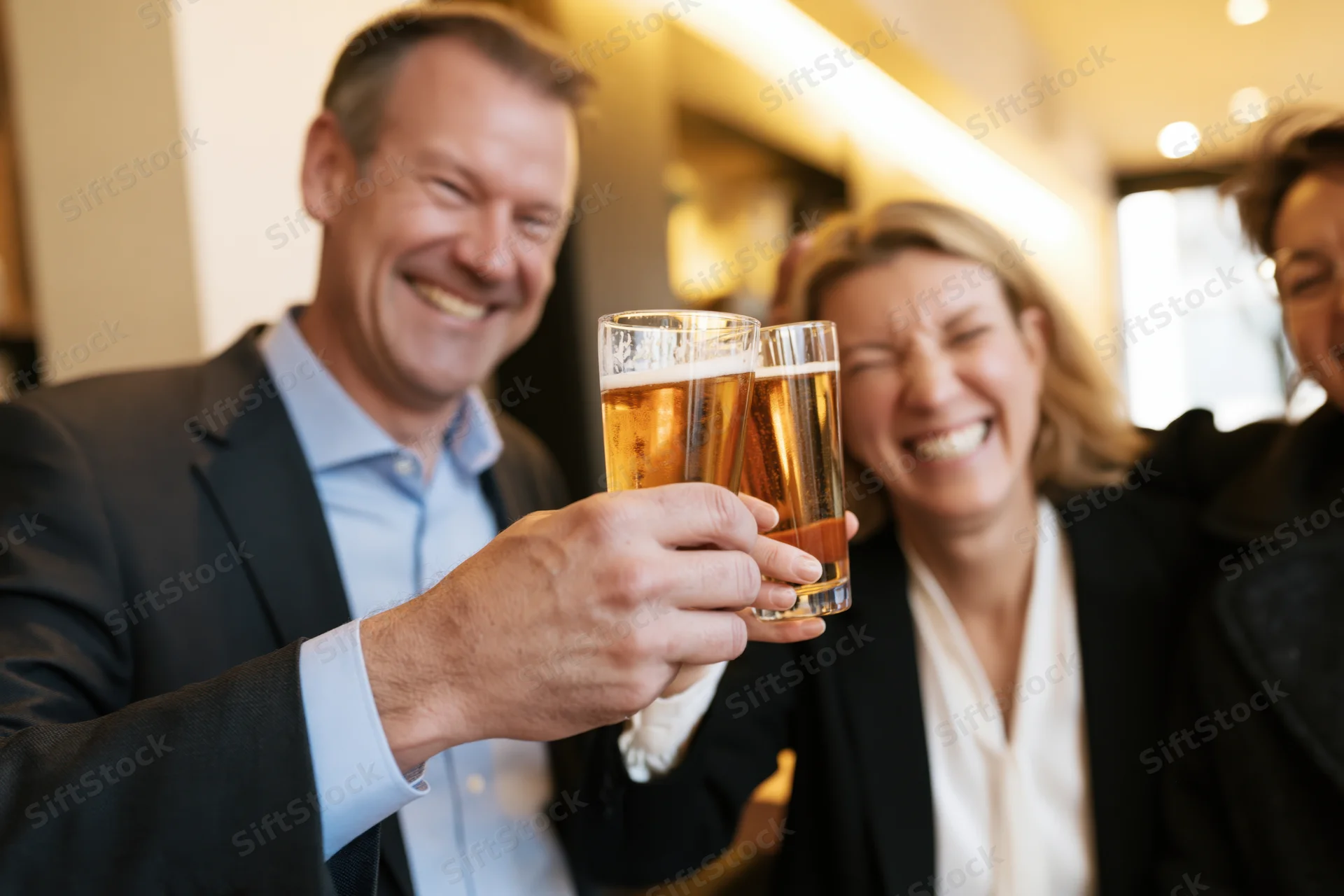 Man and woman in business attire toasting with beer glasses in an office setting