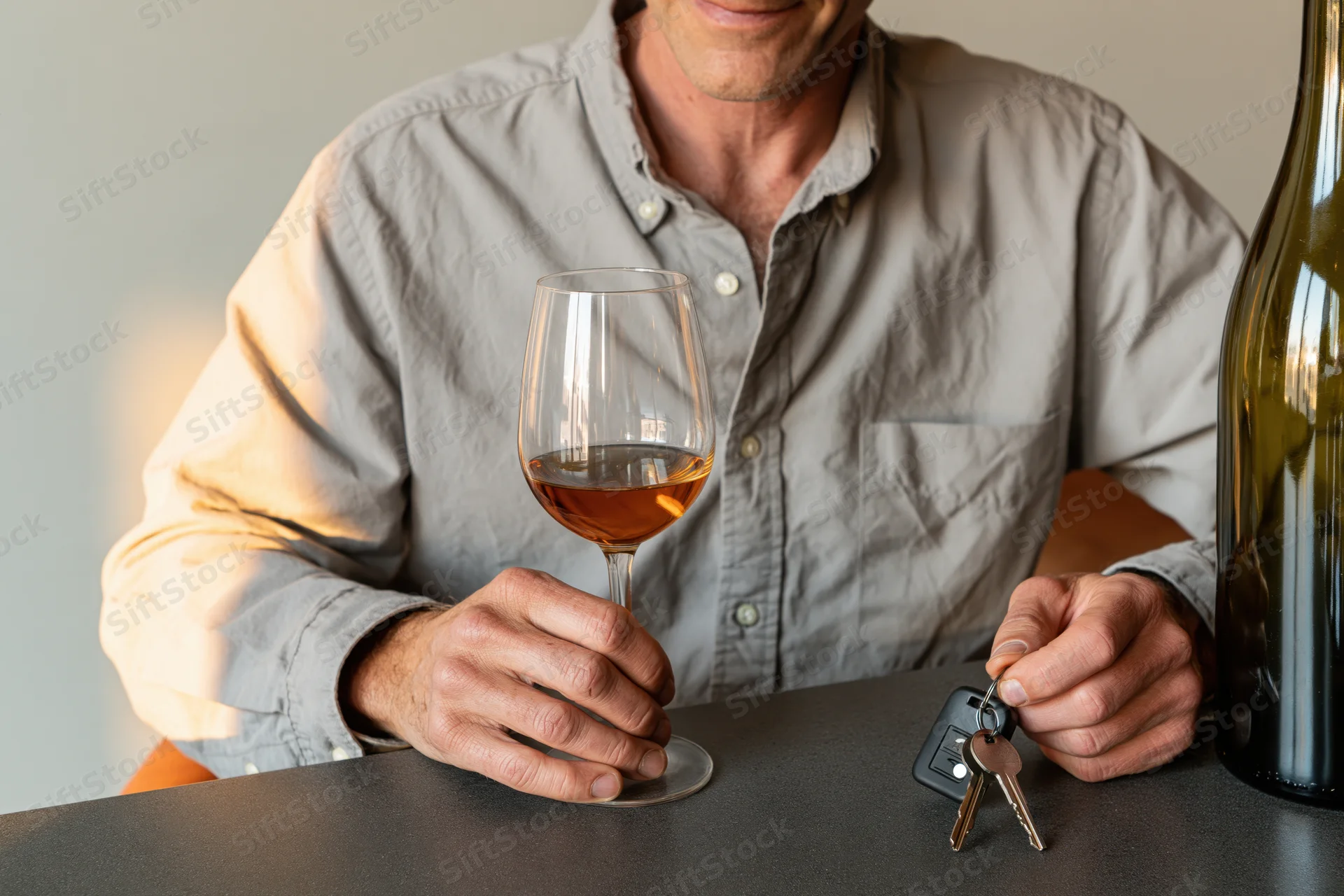 Man holding wine glass and car keys at dark gray bar table