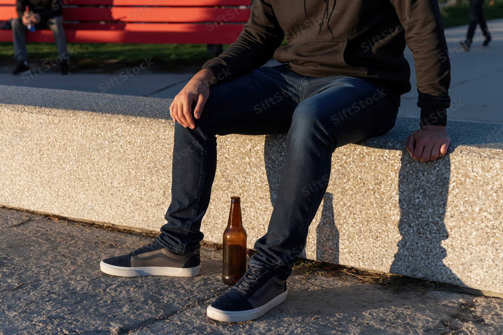 Man sitting on a concrete ledge with a beer bottle beside him in a park setting