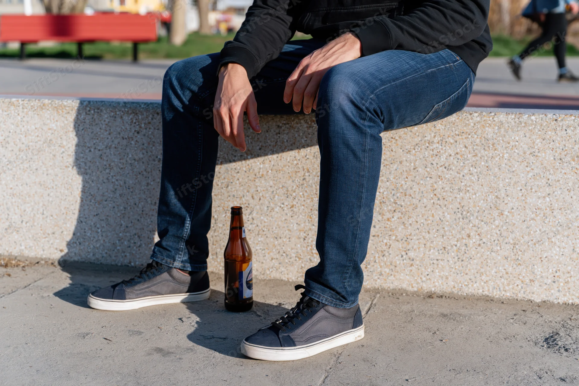 Man sitting on concrete ledge with beer bottle beside his sneakers in park setting