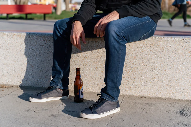 Man sitting on concrete ledge with beer bottle beside his sneakers in park setting