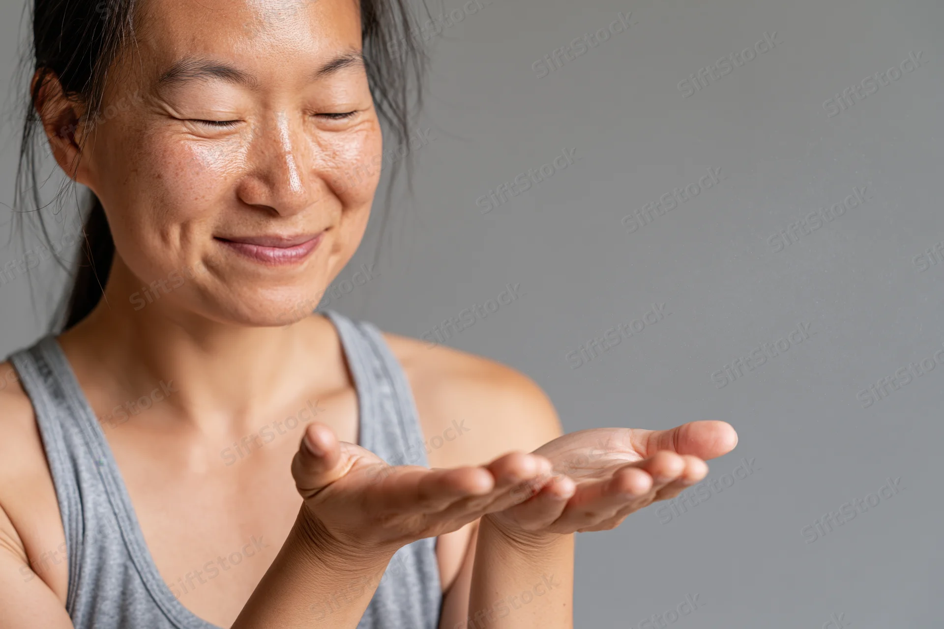 Woman smiling with hands cupped catching mist spray from sanitizer bottle