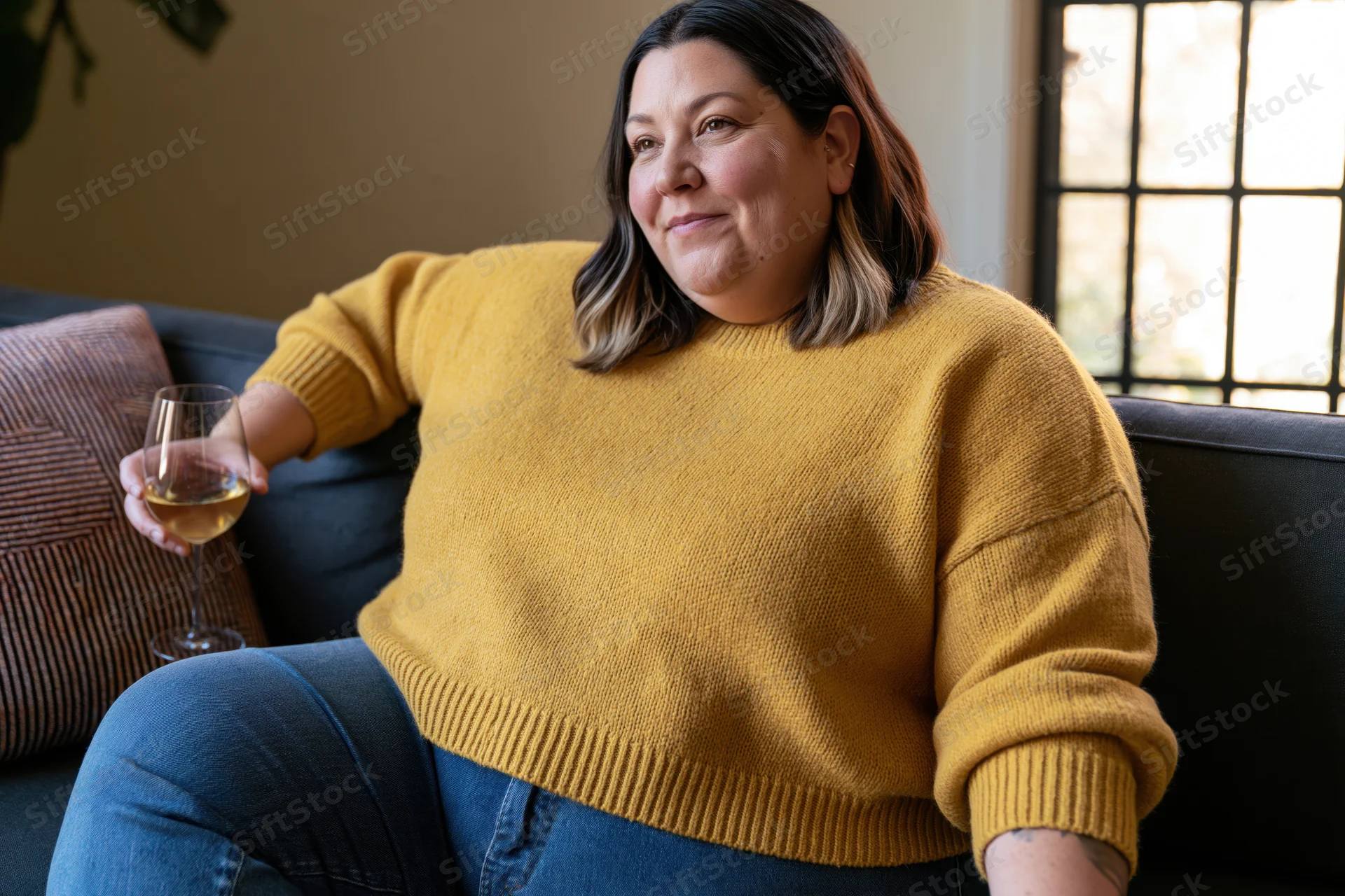 Plus-size woman sitting on sofa holding wine glass, smiling, in living room