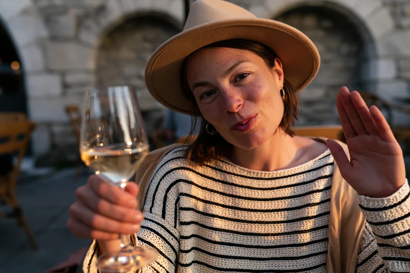 Woman holding wine glass and waving at outdoor cafe patio