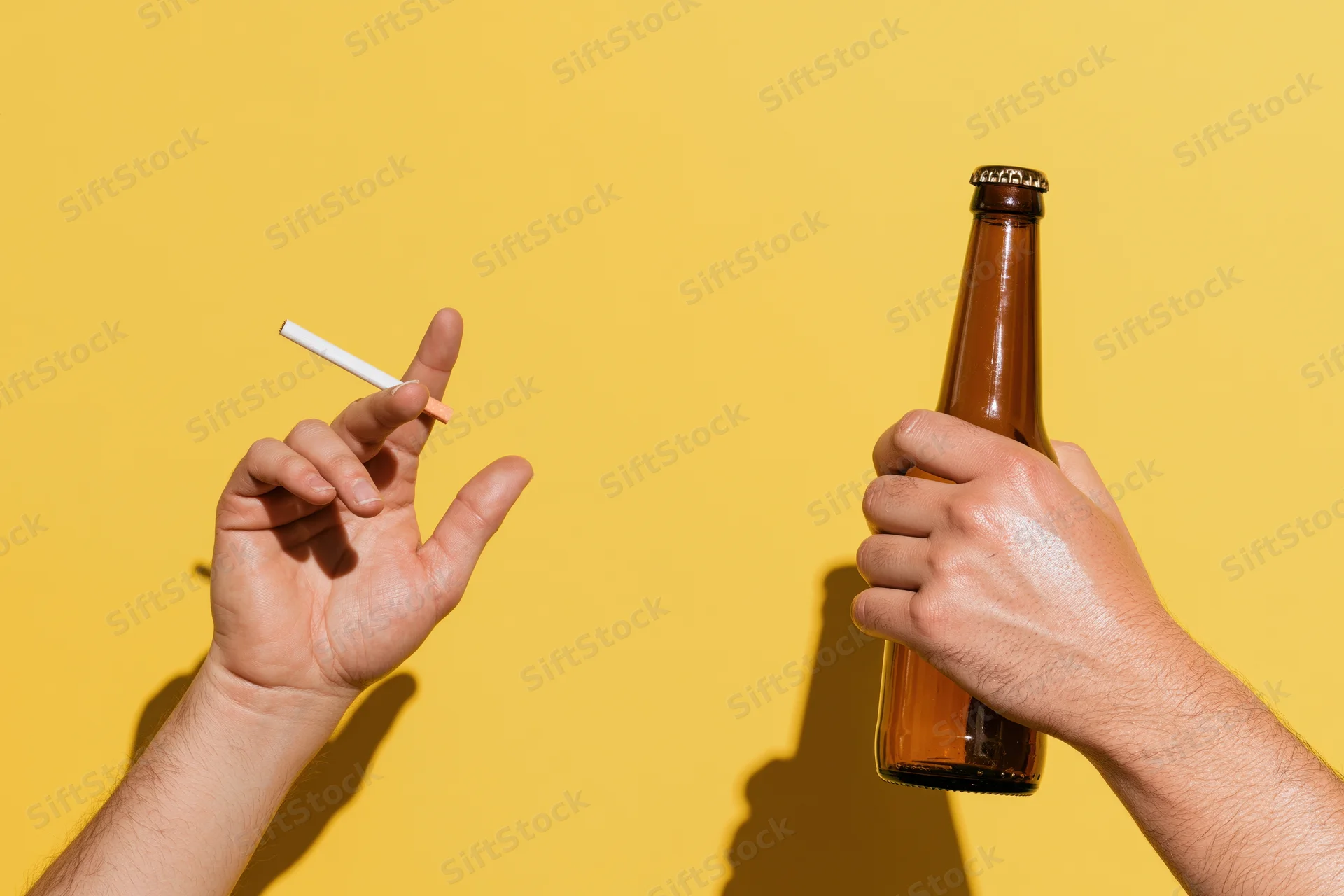 Two hands holding a cigarette and a beer bottle against a yellow background