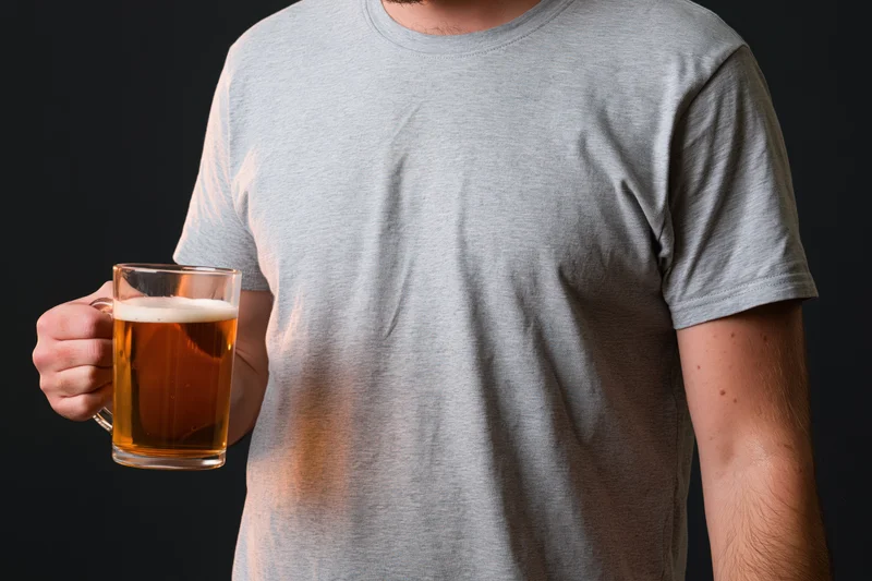 Man holding a glass mug of beer against a dark background