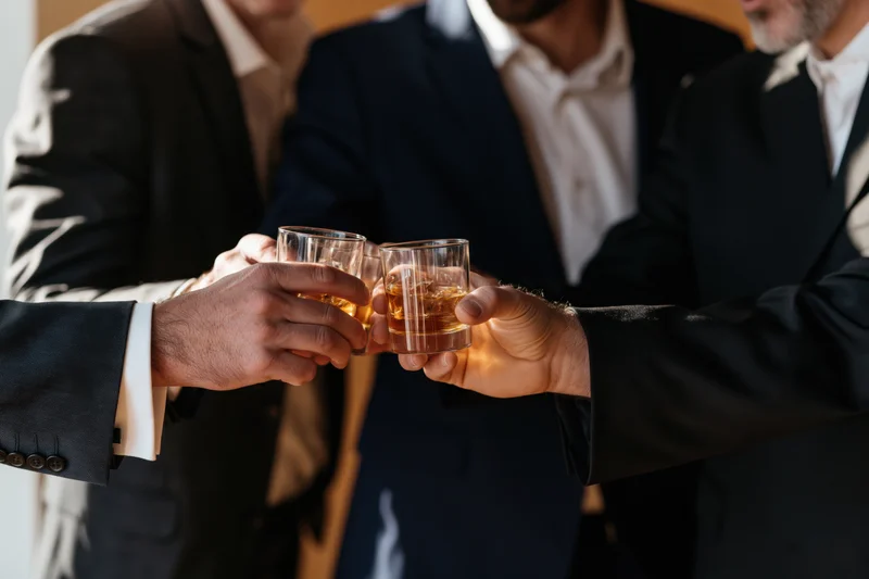Three men in business suits toasting with whiskey glasses indoors