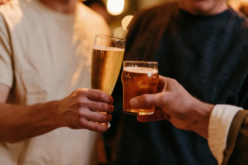 Two men toasting with beer glasses in a dim bar