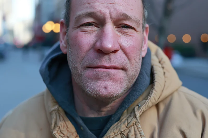 Closeup of a man in a tan hooded jacket outdoors on a city street