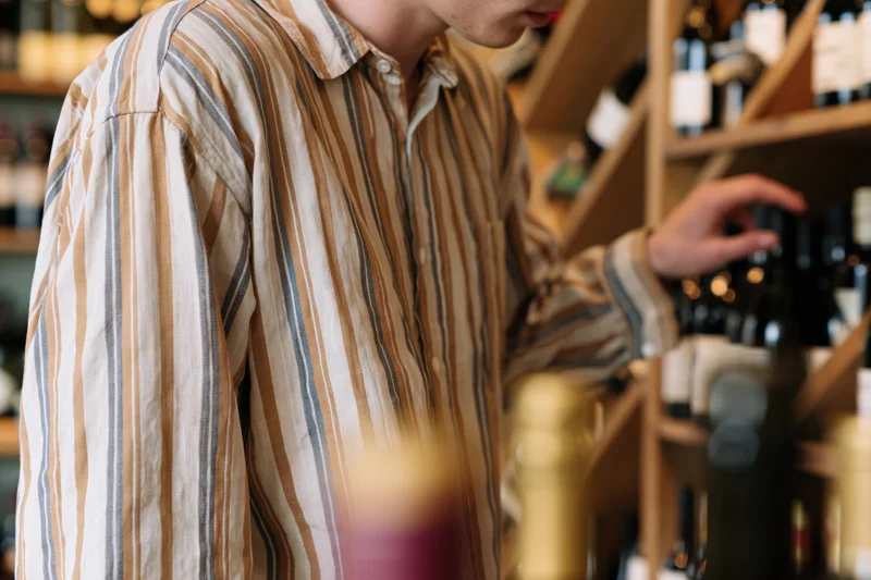 Man browsing wine bottles on wooden shelf in shop