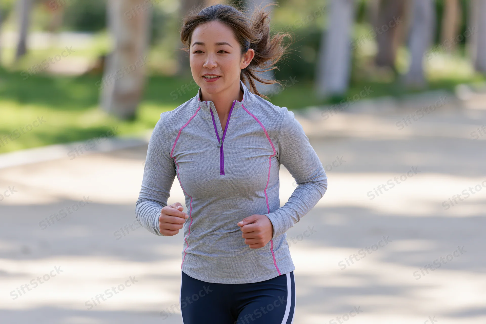 Asian woman running on paved path in park surrounded by trees during daylight