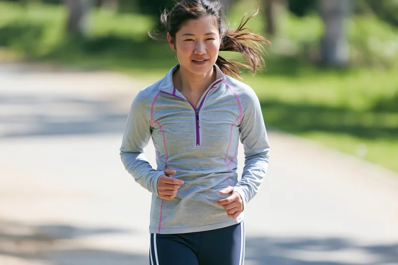 Asian woman running on a paved path in a park during daylight