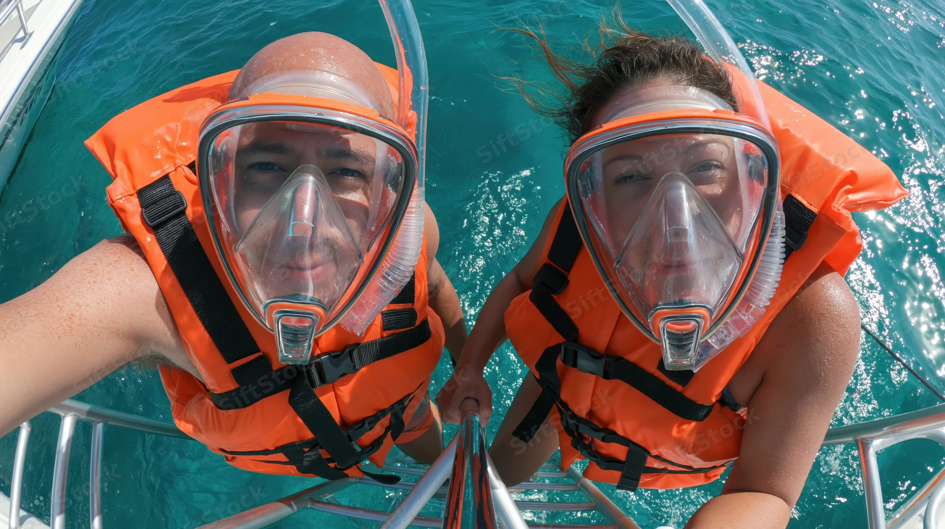 Two snorkelers in orange lifevests and masks climbing a metal ladder into the ocean