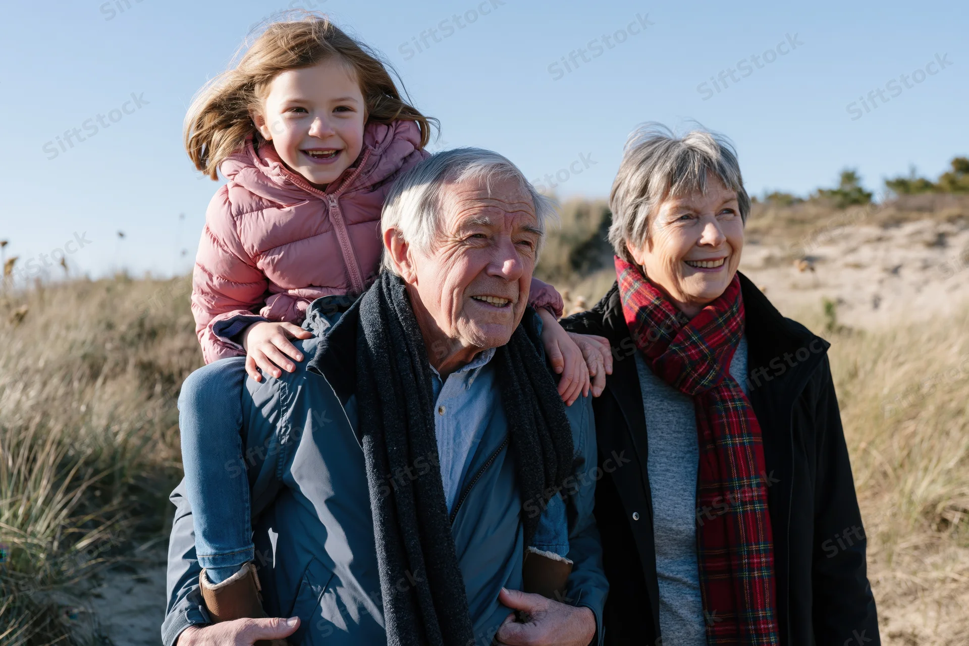 Grandparents carrying granddaughter on shoulders on a sunny coastal trail