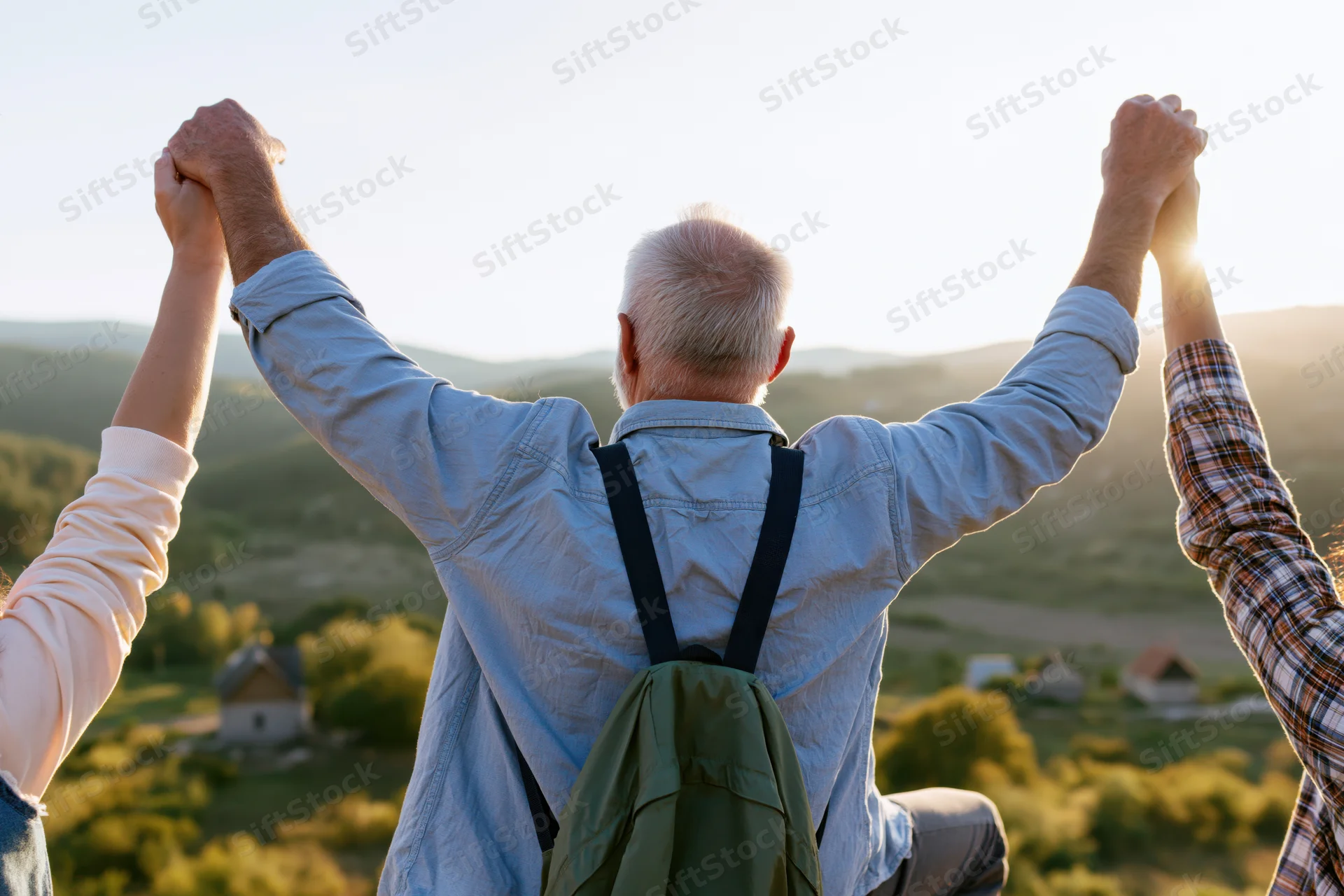 Senior man with arms raised holding hands with two people overlooking a countryside valley at sunset