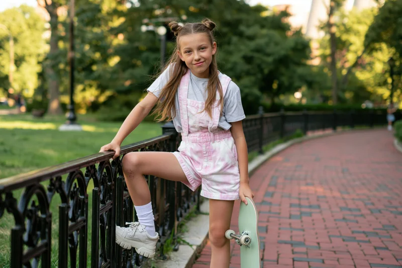 Young girl leaning on a black metal railing with a skateboard in a park