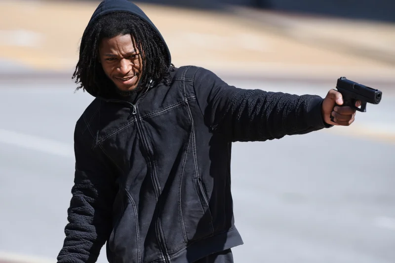 Man in black hooded jacket pointing handgun outdoors on street