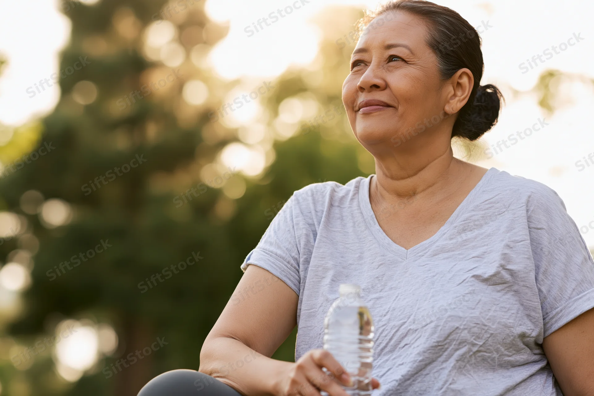Senior asian woman sitting outdoors holding water bottle in soft natural light