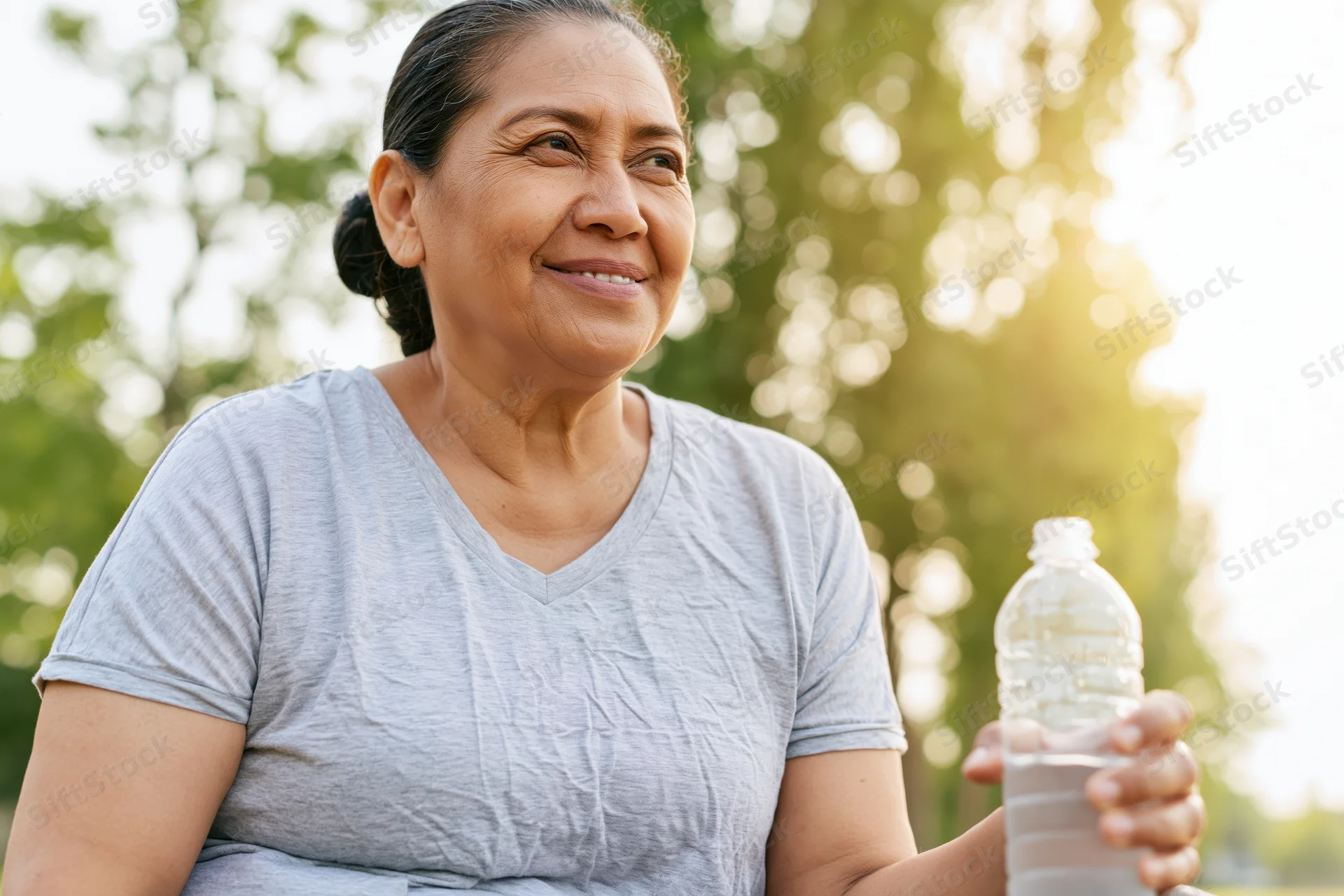 Senior woman holding water bottle outdoors in park during golden hour smiling