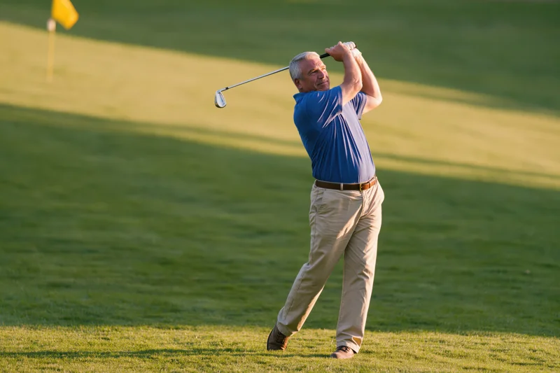 Middle-aged man swinging golf club on green golf course during golden hour