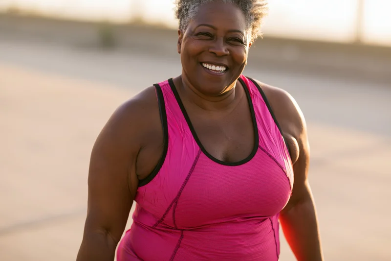 Smiling senior black woman in pink athletic tank top exercising outdoors on pavement