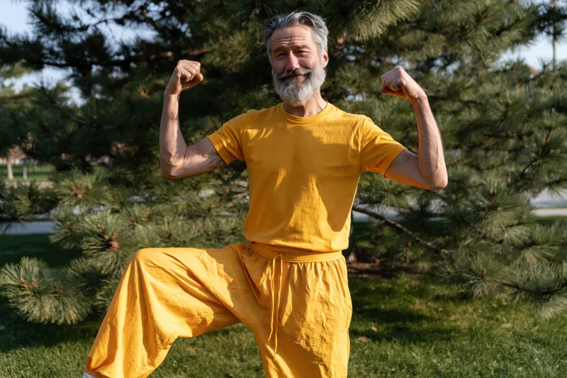 Senior man flexing biceps in yellow outfit in park setting