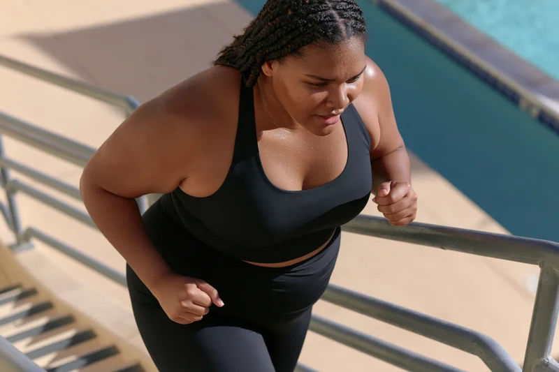 Plus-size black woman exercising on poolside stairs in sportswear during daytime