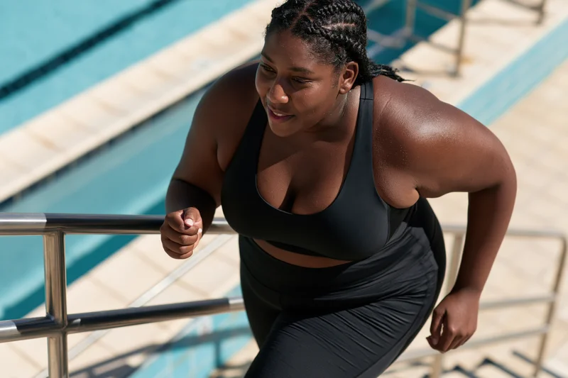 Plus-size black woman climbing steps out of swimming pool in sportswear