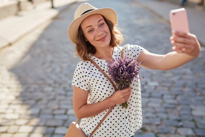 Young woman taking selfie with lavender bouquet on cobblestone street