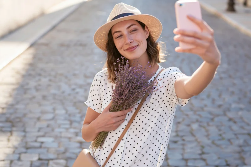 Young woman taking selfie with lavender bouquet on cobblestone street