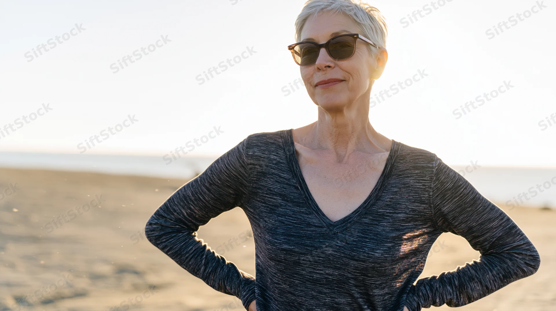 Senior woman standing on beach with hands on hips at sunset