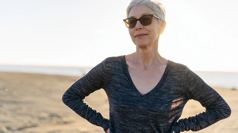 Senior woman standing on beach with hands on hips at sunset