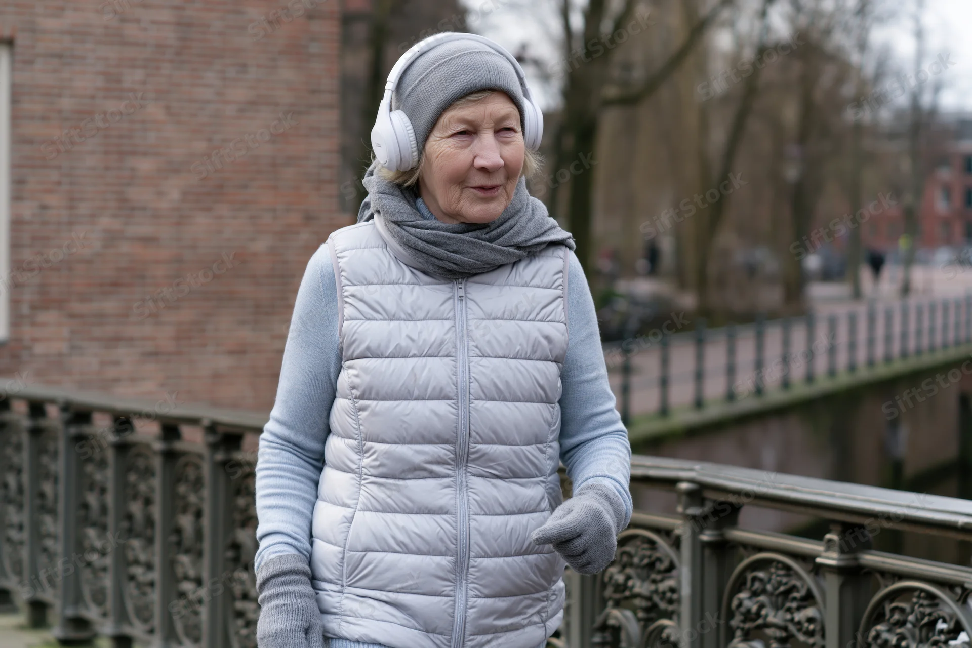 Elderly woman walking outdoors on a bridge wearing headphones and winter clothing