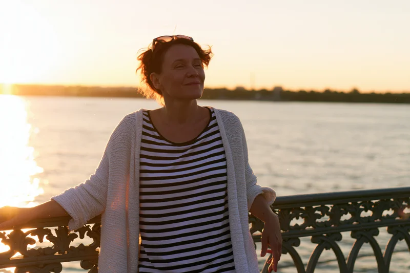 Woman leaning on decorative iron railing by waterfront at sunset