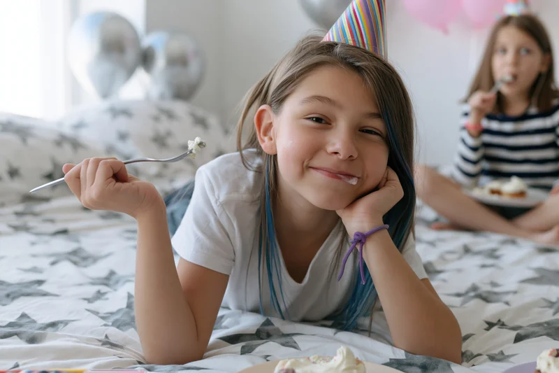 Girl smiling with fork and cake crumbs on bed at birthday party