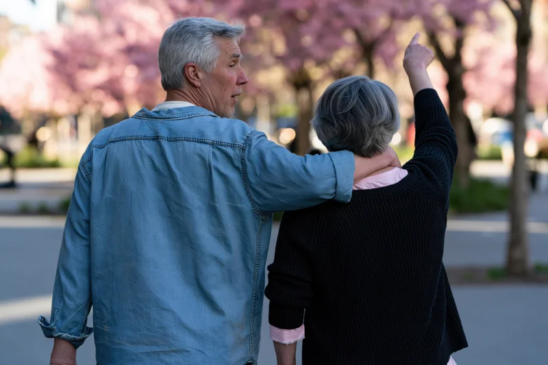 Older couple walking arm-in-arm in a park with cherry blossoms in spring