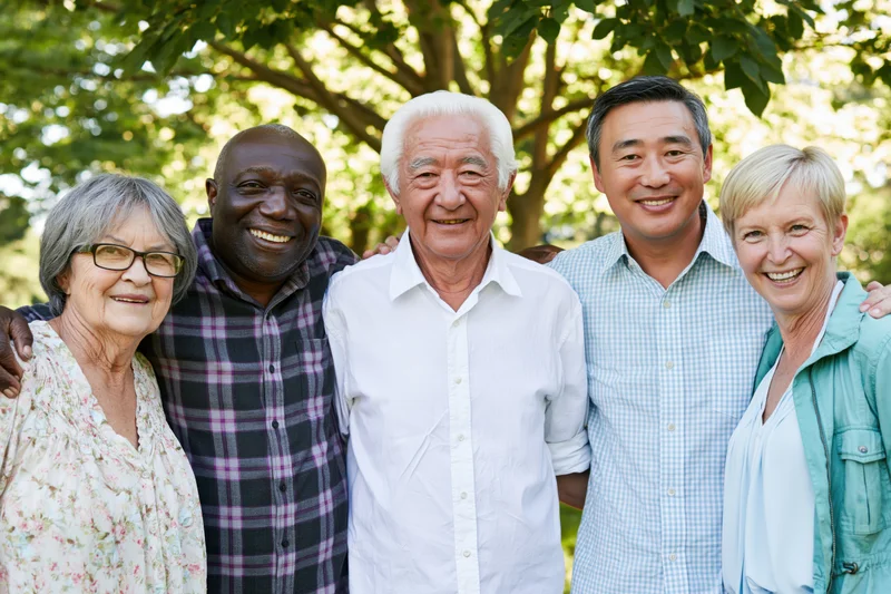 Five smiling seniors posing together in a park under leafy trees