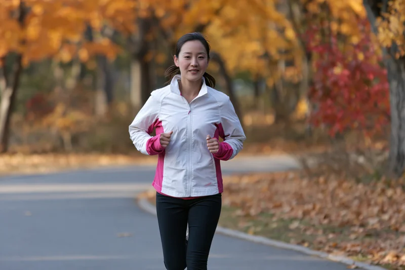 Asian woman running on a paved path in an autumn park
