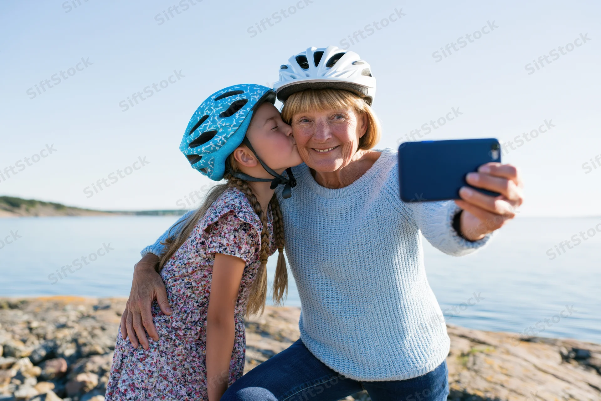 Grandmother and granddaughter taking a selfie by the water while wearing cycling helmets