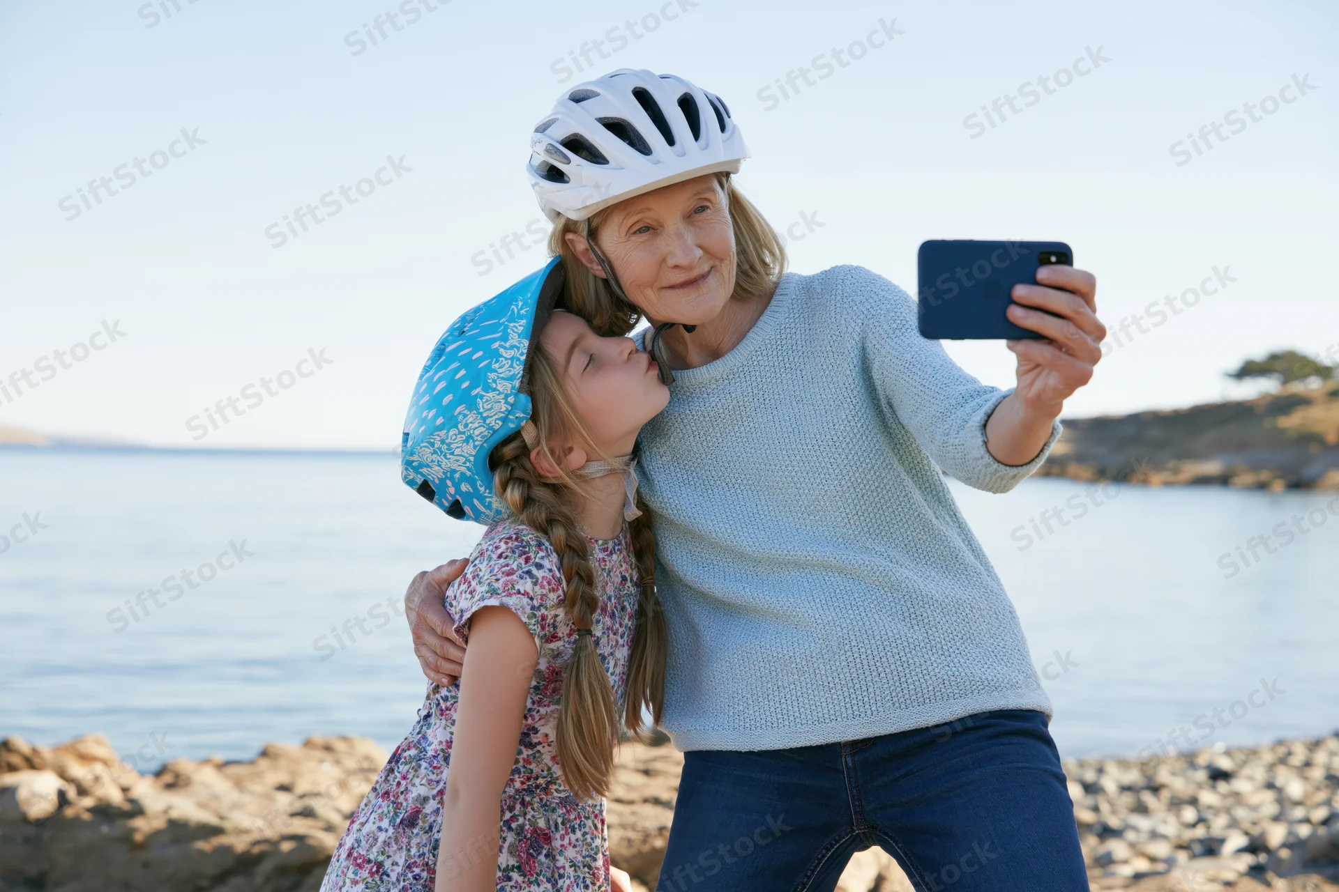 Grandmother and granddaughter taking a selfie together on a rocky beach by the ocean