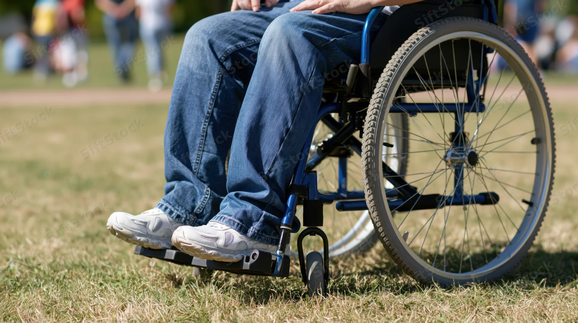 Person in wheelchair on grass in park, close-up view of legs and wheels