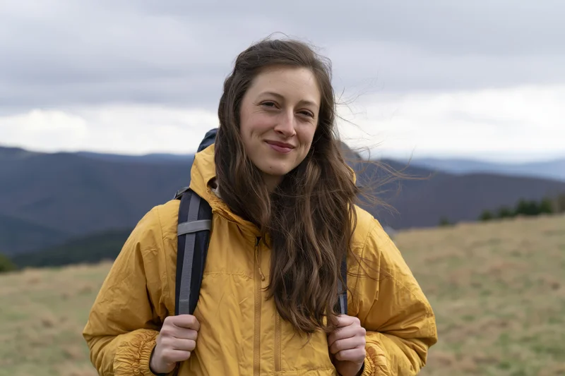 Young woman smiling while hiking in a mountainous field with backpack and yellow jacket