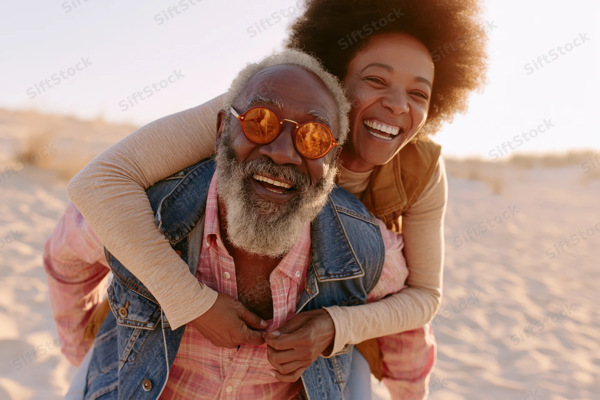 Older interracial couple laughing while piggybacking on a sandy beach at golden hour