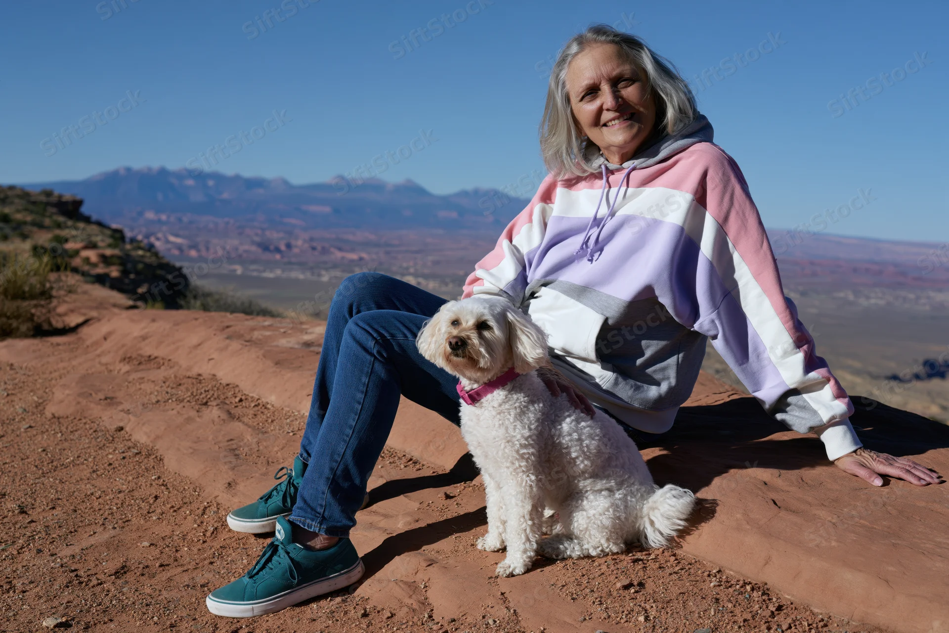 Senior woman smiling with small white dog on red rock canyon trail