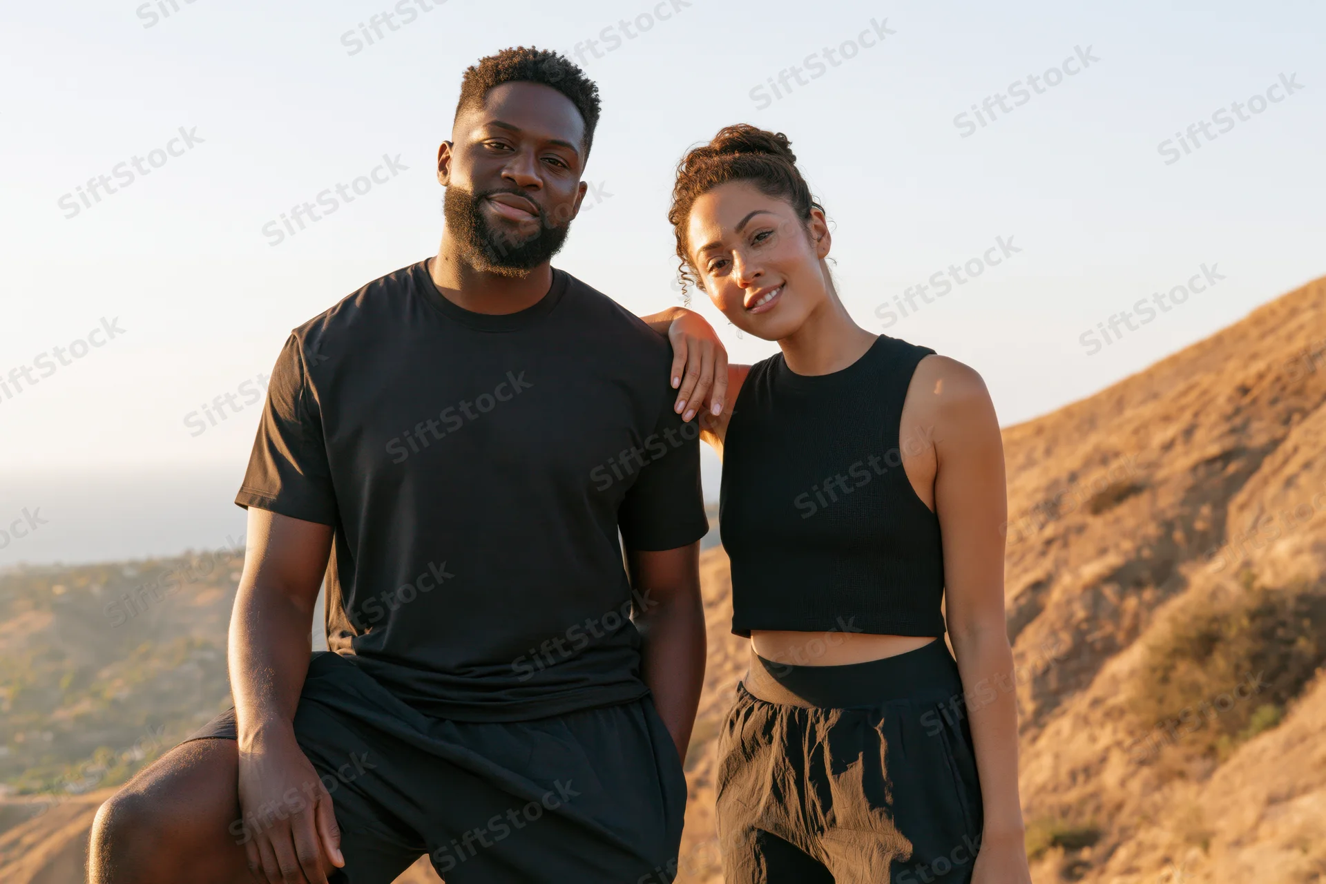 Couple posing together on a sunlit hillside in athletic wear